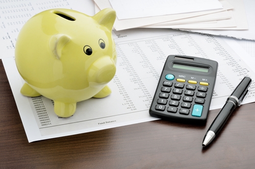 There is a green piggy bank on top of a desk, along with a calculator and papers.