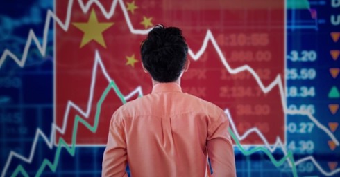 A man looking at the fluctuating prices of the stock market with a Chinese flag in the background.