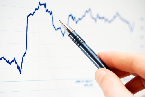 A hand is working on drawing a trend line with a blue ink pen on white paper.