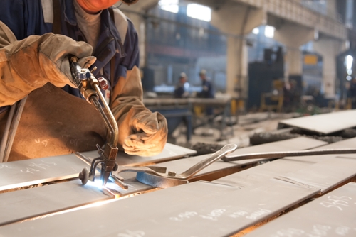 A picture of an employee in a factory welding a large piece of metal.