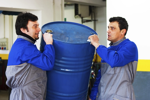 Two male employees are carrying a large barrel of oil.
