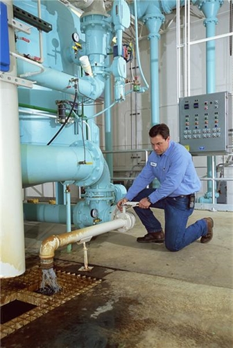 A ,ale employee dressen in blue works to fix a complex system inside a manufacturing facility.