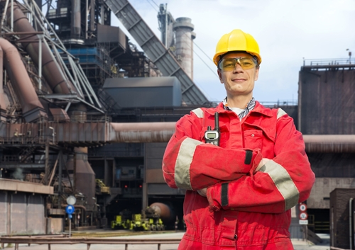 There is a proud employee at a manufacturing facility dressed in a bright red jumpsuit.