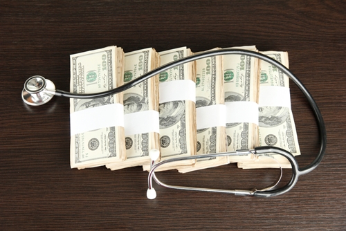 A picture of a stethoscope placed over many dollar bills symbolizing how the manufacturing of medical devices is quite expensive.