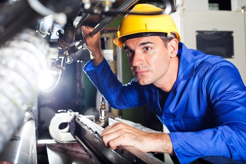 A male employee looking deeply into the mechanisms within factory machinery.