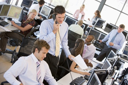 A picture of many young stock-brokers talking on the phones and making deals while working in an office.