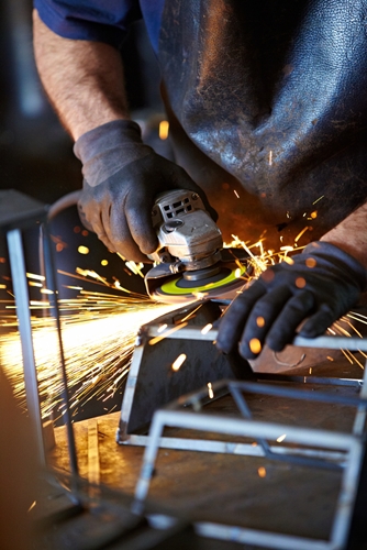 An employee is a factory works to shave the edges of part made from metal.