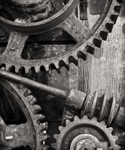 A view at oversized gray gears turning together to manufacture something.