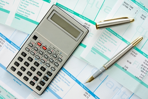 A desk with several accounting ledgers as well as a calculator and a pen.