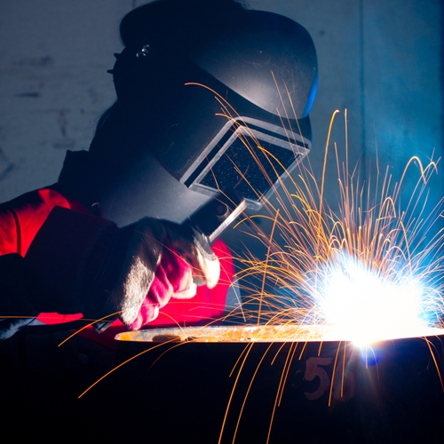 A man with a large face mask works on welding a from of a metal.