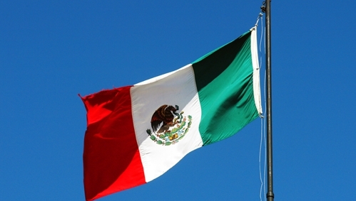 A picture of the Mexican flag waving in the blue Mexican sky.