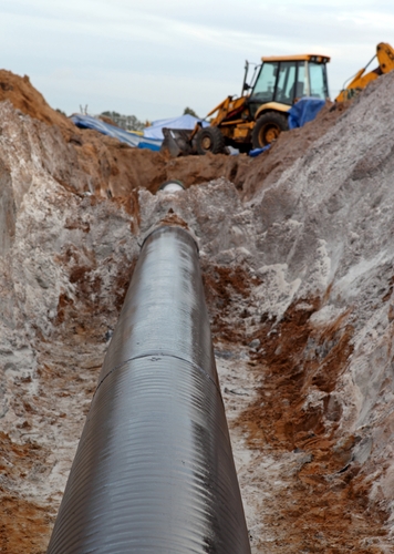 A view of a pipeline that is surrounded by dirt and a tractor.