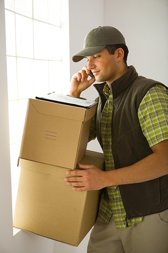 A man works to transport two large boxes from one place to another while talking on the phone.