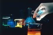 There are several flasks that contain chemicals in the background, while a scientist works to begin a chemical reaction.