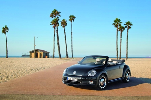 A view of a Volkswagen car in the middle of a sandy beach with palm trees in the background.